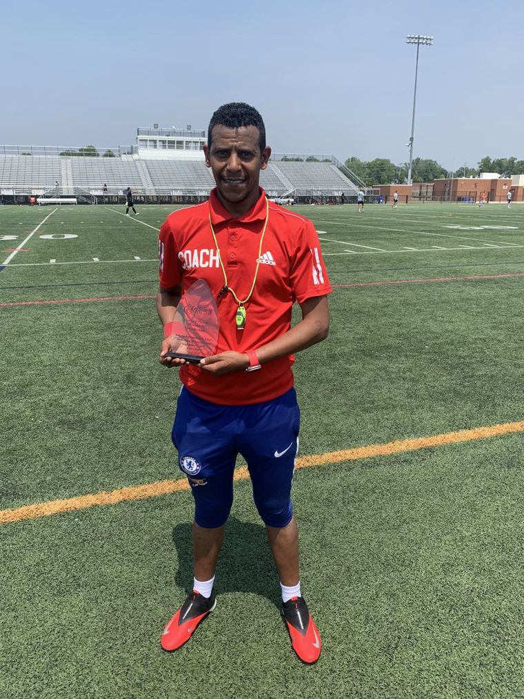 Coach Awet Berhane holding a coaching award on the field