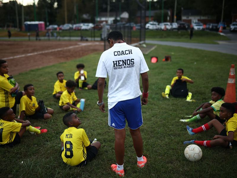 A group of young players seated on the grass listening to Coach Awet
